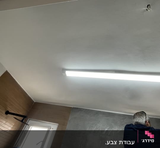 אדם צובע תקרה בחדר עם תאורה פלורסנטית